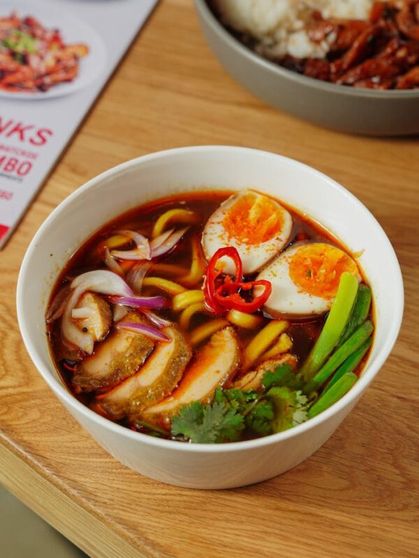 Close-up of a flavorful Asian ramen bowl topped with boiled eggs, vegetables, and chili.
