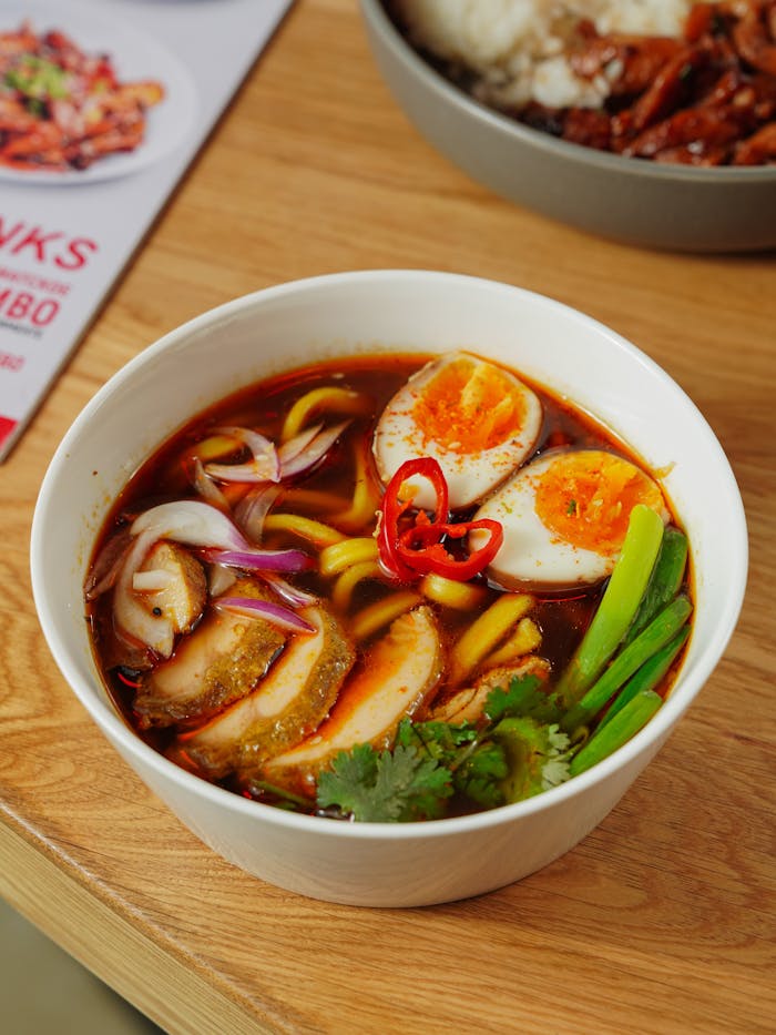 Close-up of a flavorful Asian ramen bowl topped with boiled eggs, vegetables, and chili.