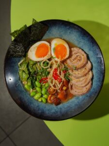 Top view of a flavorful ramen bowl with egg, sliced pork, greens, and noodles.