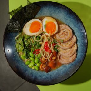 Top view of a flavorful ramen bowl with egg, sliced pork, greens, and noodles.