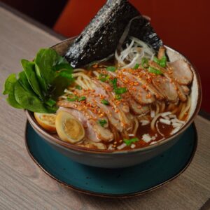 A flavorful bowl of Japanese ramen with sliced pork, egg, and seaweed, ideal for food enthusiasts.